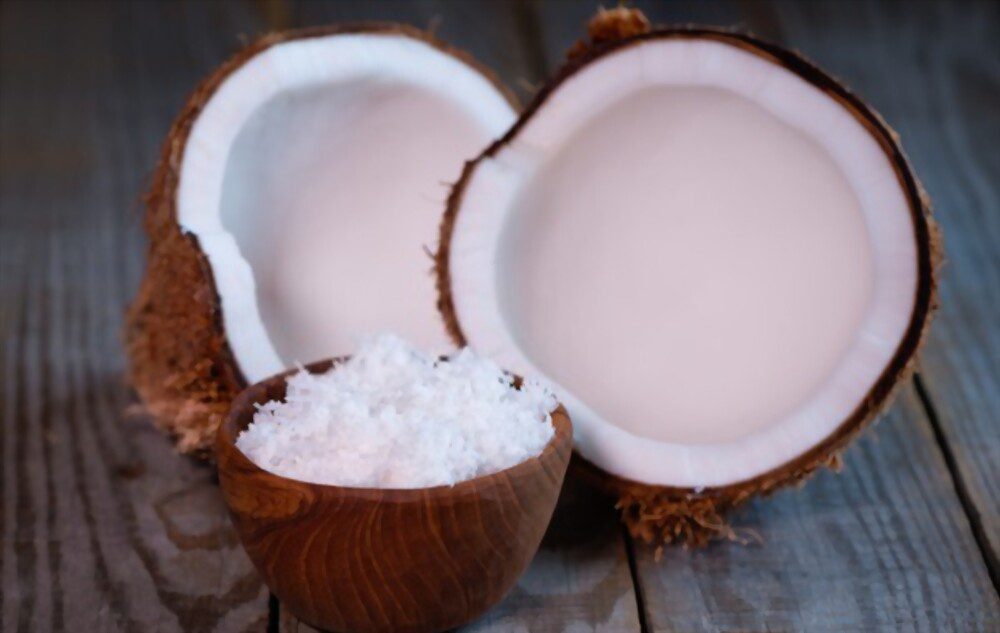 Coconut split in two halves and coconut flakes in wooden bowl