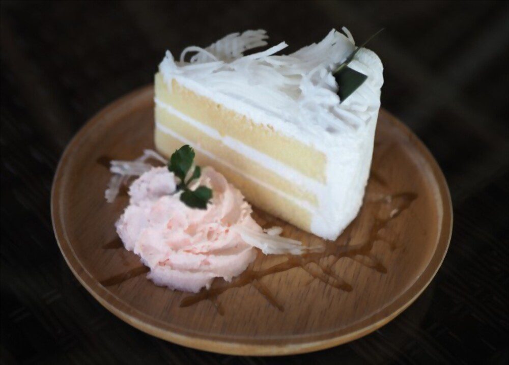 Coconut cake with whipped cream on wooden plate.