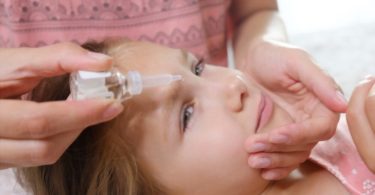 Mother dripping allergy eye drops for kids in girl's eyes.