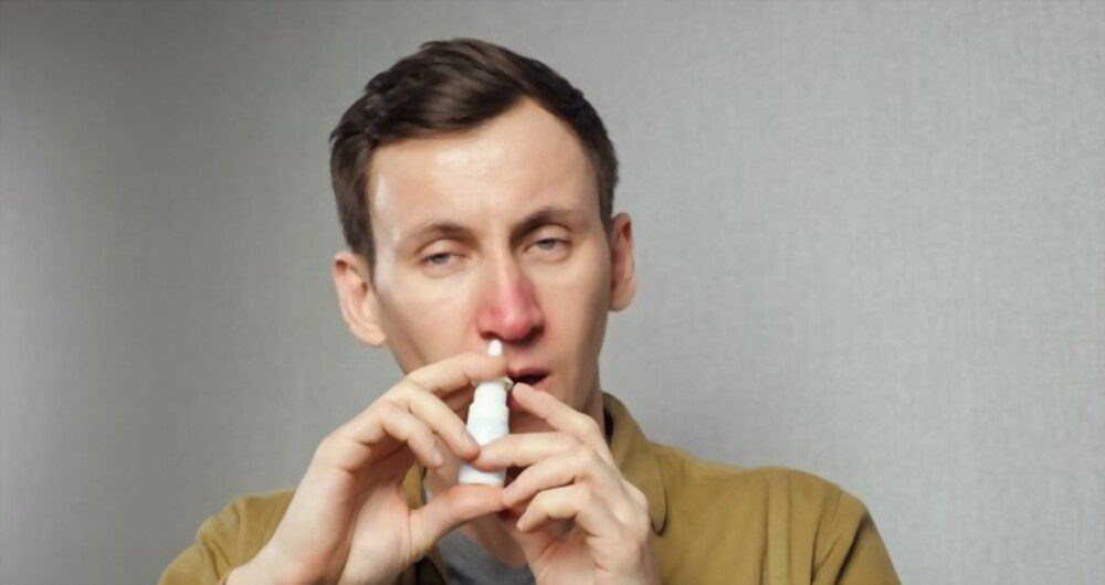 An allergic man spraying the nasal medication into nostrils to get relief from respiratory allergies.