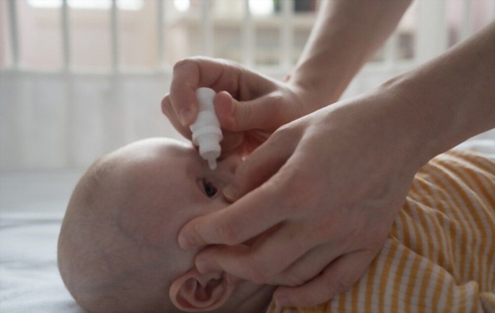Mother is treating newborn eye inflammation by dripping allergy eye drops for kids.