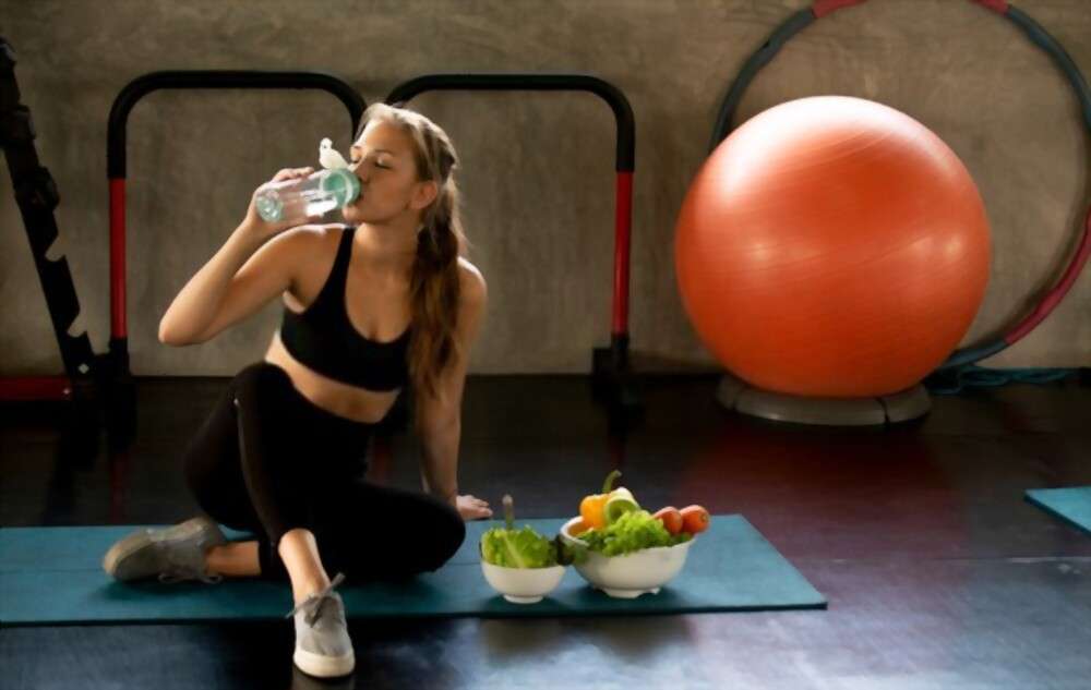A woman drinking water in gym and using agoge diet plan.