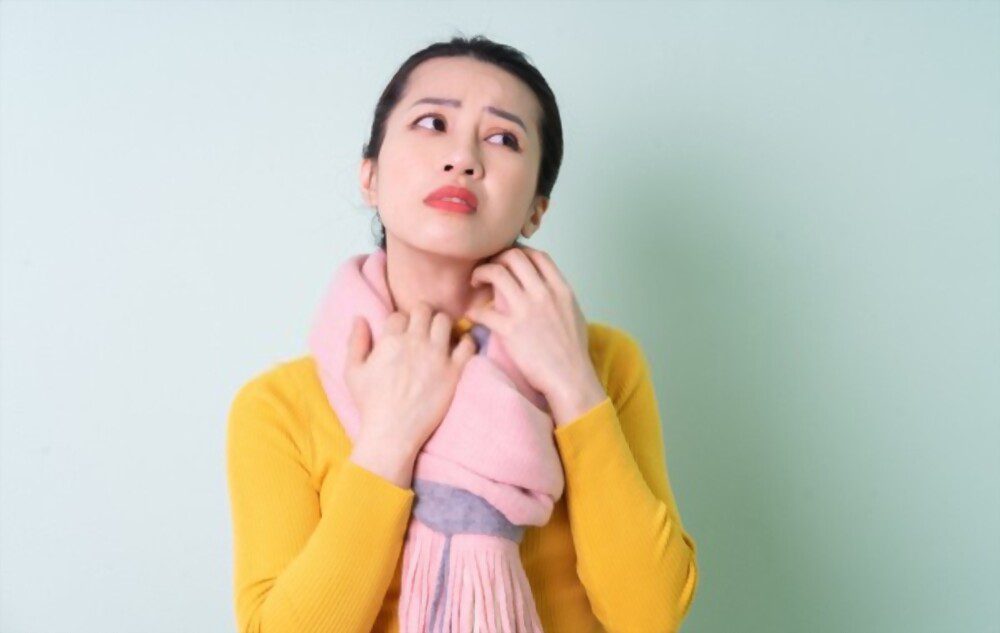 Woman wearing a wool scarf itching her neck due to wool allergy